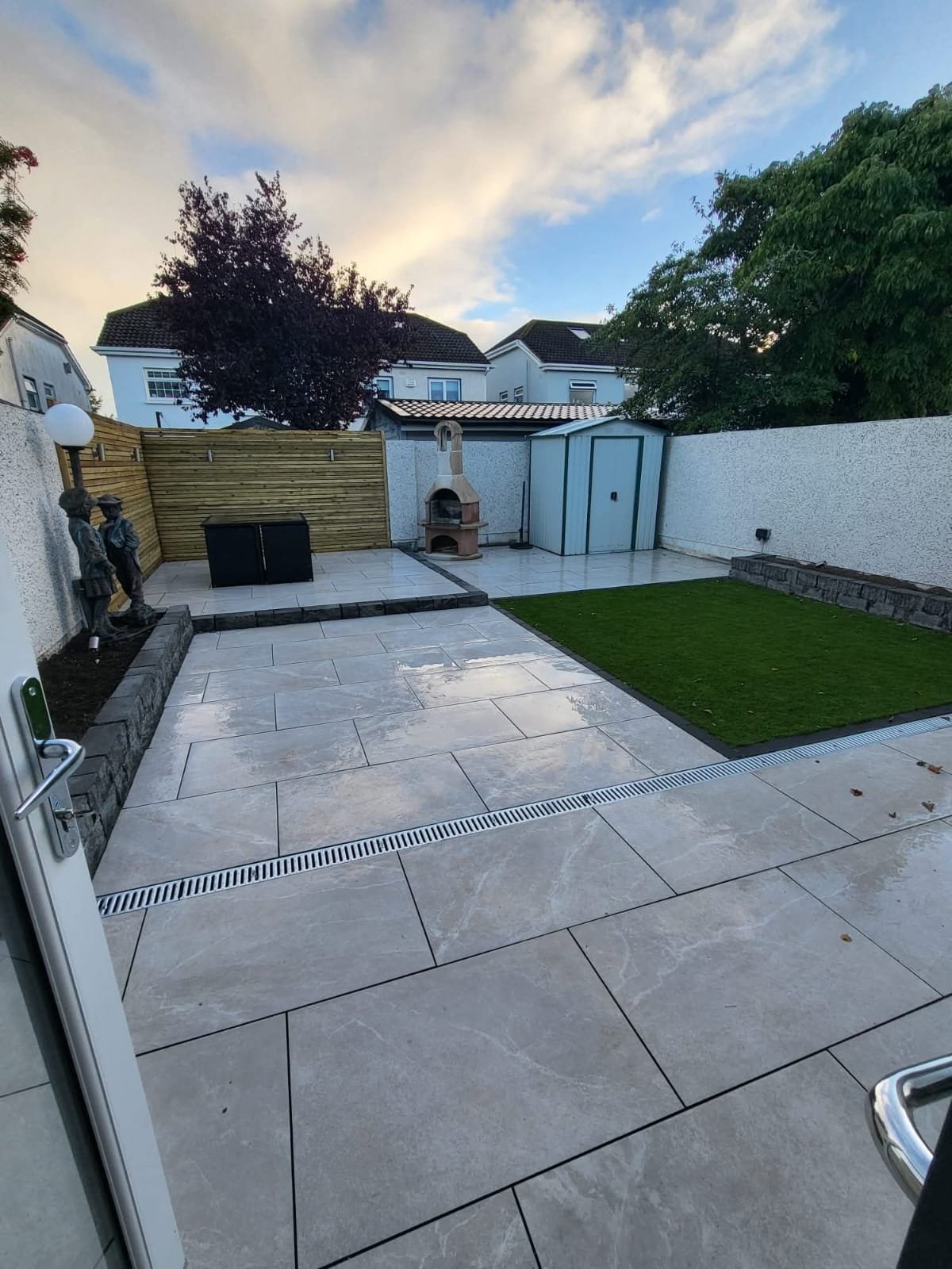 Patio Design with fake grass, tiling and small shed by Green Capital Landscaping and Gardening