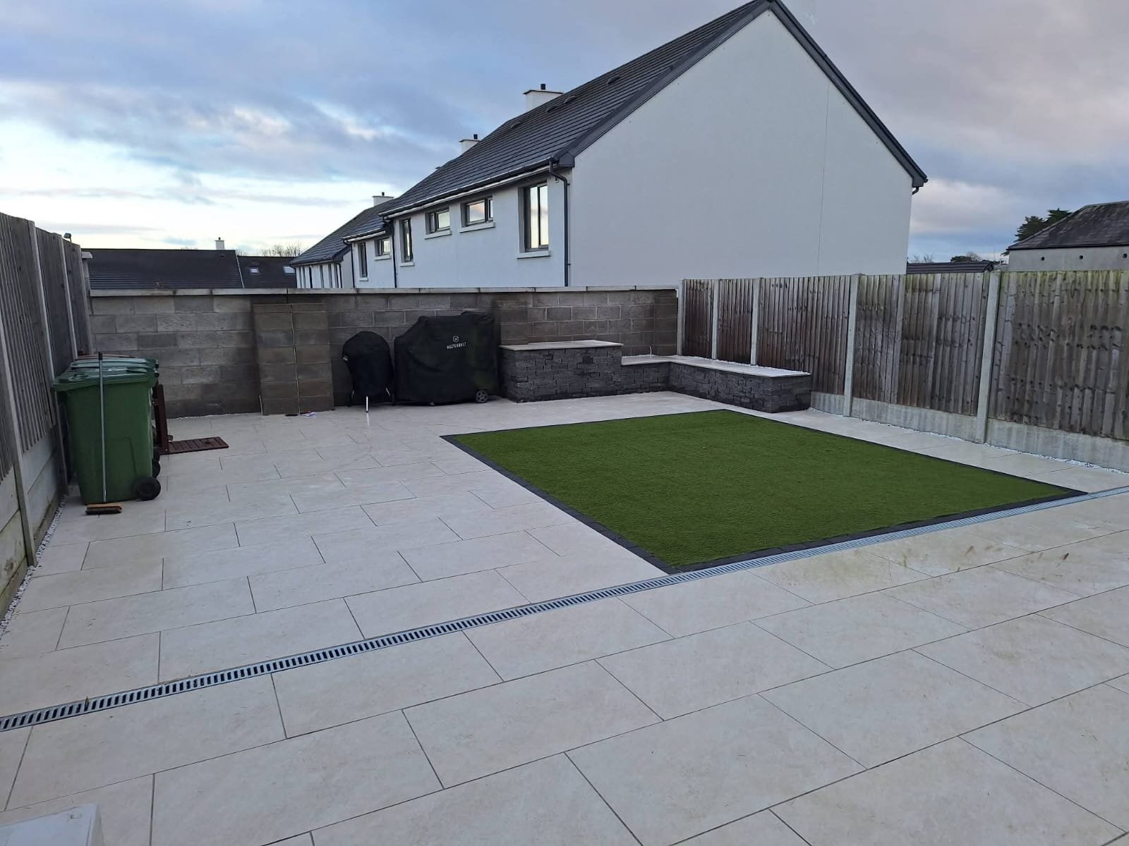 Patio Design with fake grass and seating area and bin storage by Green Capital Landscaping and Gardening